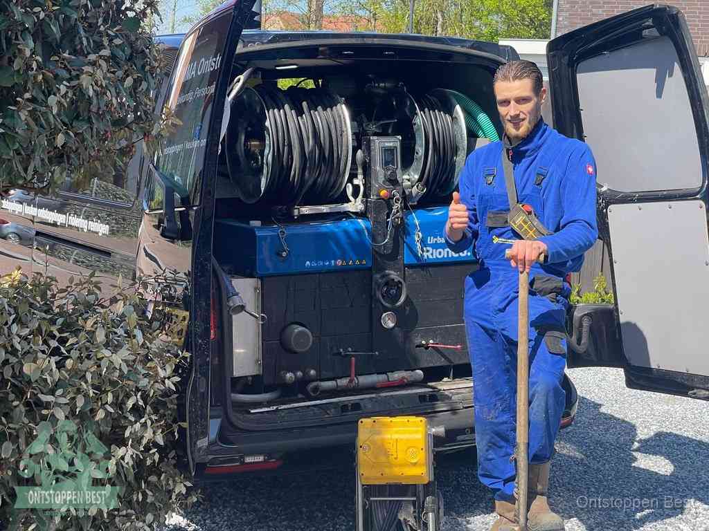Lachende monteur bij de volle rioolreinigingsbus, een professioneel rioolontstoppingsbedrijf in Best