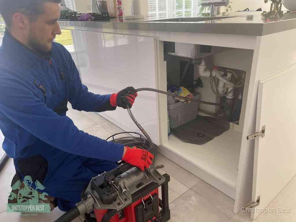 Monteur voert een ontstoppingsveer in de afvoer onder de keuken in Best