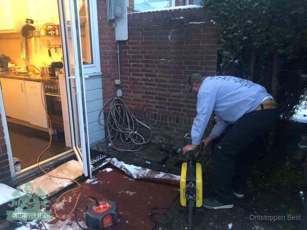 Een monteur werkt buiten bij een open riool-/grondput met een elektrische ontstoppingsmachine om een verborgen afvoerprobleem op te sporen in Best