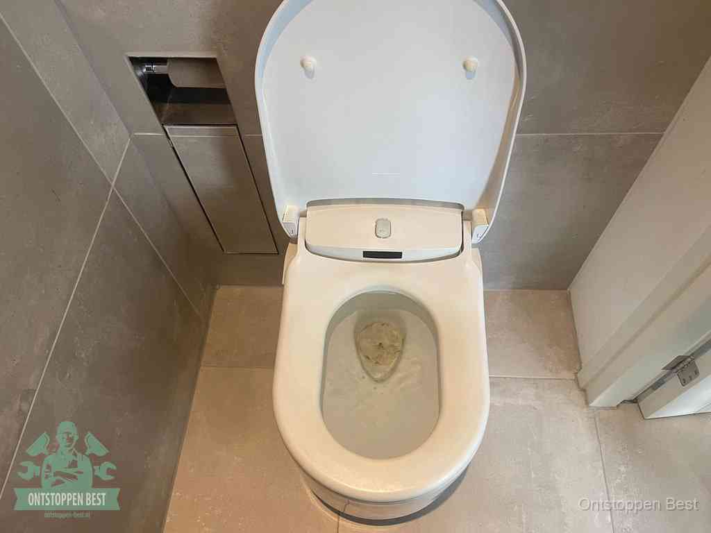 Een wit hangtoilet waarin een prop wc-papier op het water blijft drijven, een duidelijk signaal van een verstopte wc in Best