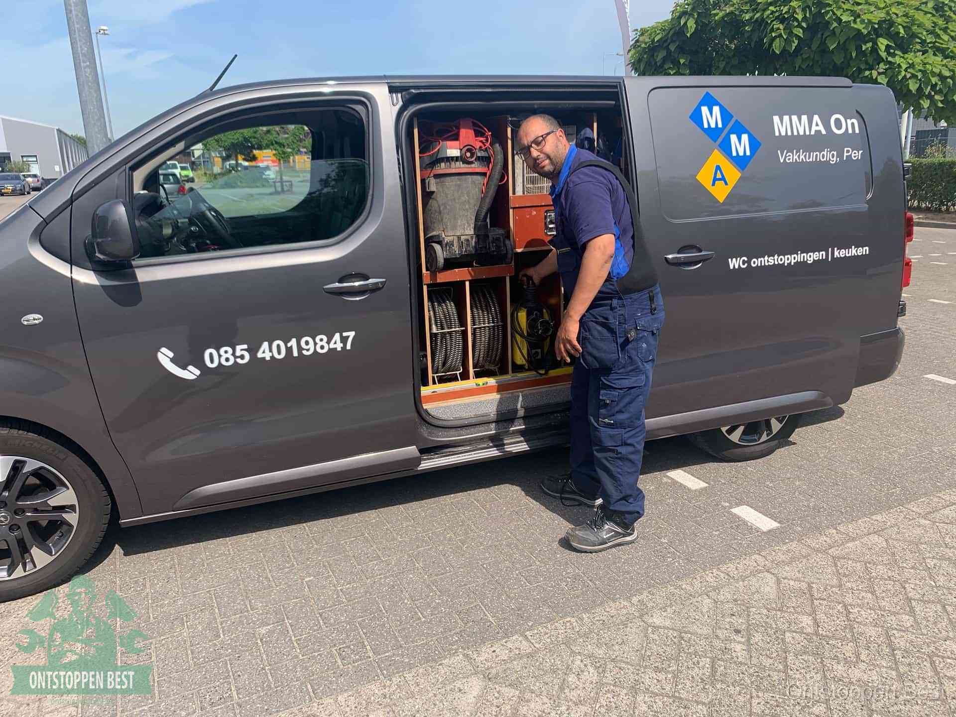 Een monteur bij de open schuifdeur van zijn bedrijfsbus op een parkeerplaats, klaar om de oorzaak van terugkerende afvoerverstoppingen aan te pakken in Best