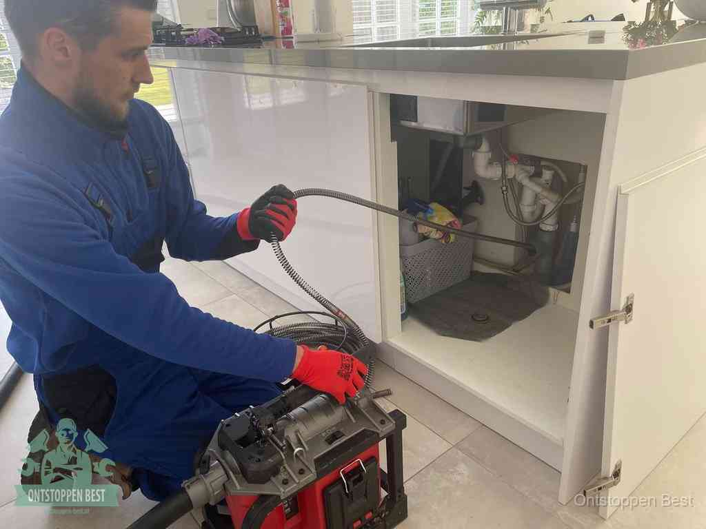 Een monteur reinigt de keukenafvoer grondig met een veermachine om terugkerende gootsteenverstoppingen te voorkomen in Best