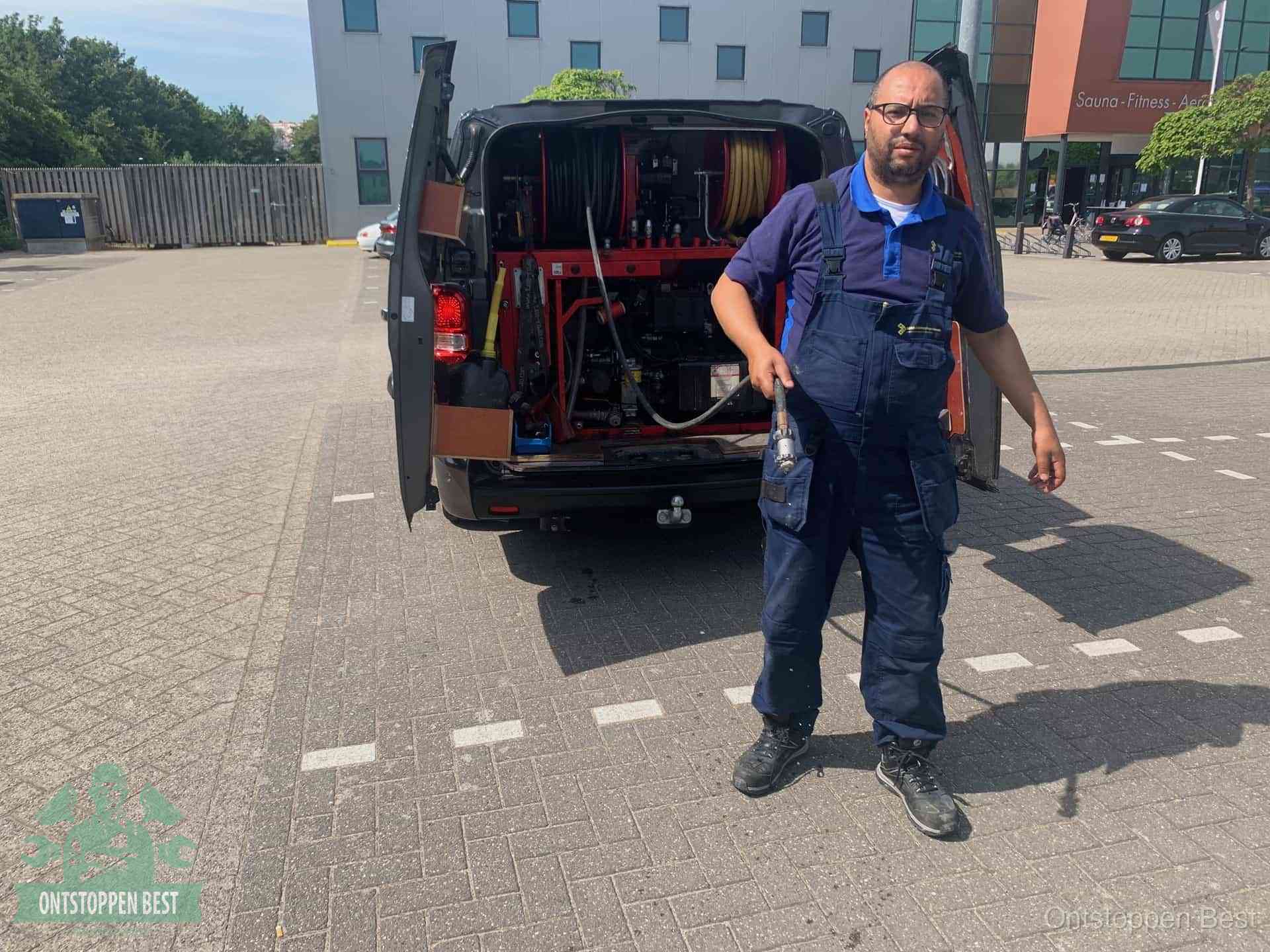 Een monteur bij zijn bestelbus met een hogedruk- en rioolreinigingsunit, klaar om de oorzaak van terugkerende wc-verstoppingen aan te pakken in Best