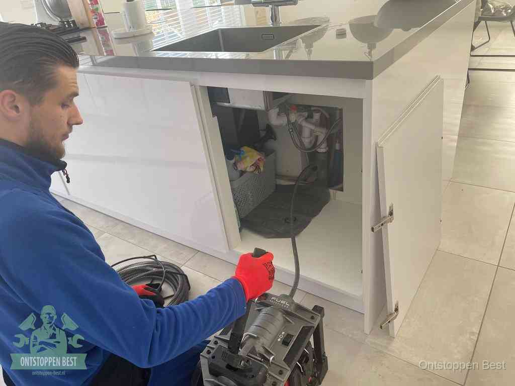 Monteur ontstopt met een veermachine een verstopte afvoer onder de gootsteen in Best