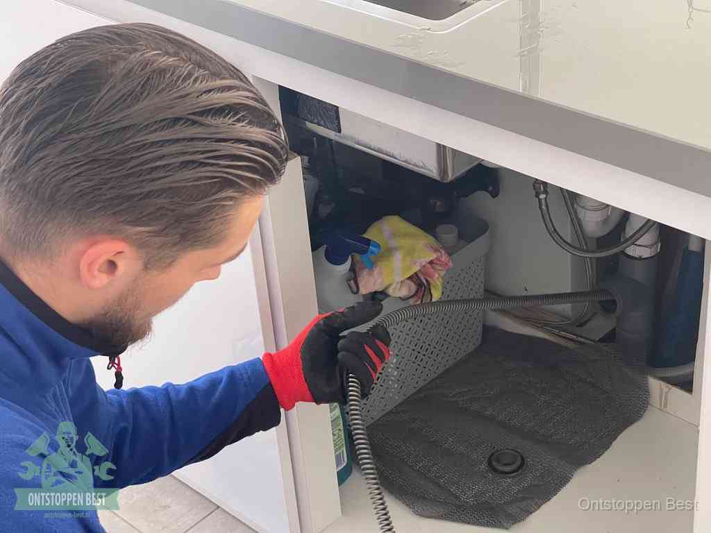 Een monteur voert een flexibele ontstoppingsveer in de afvoer om een verstopping voorbij de bocht van het toilet te bereiken in Best