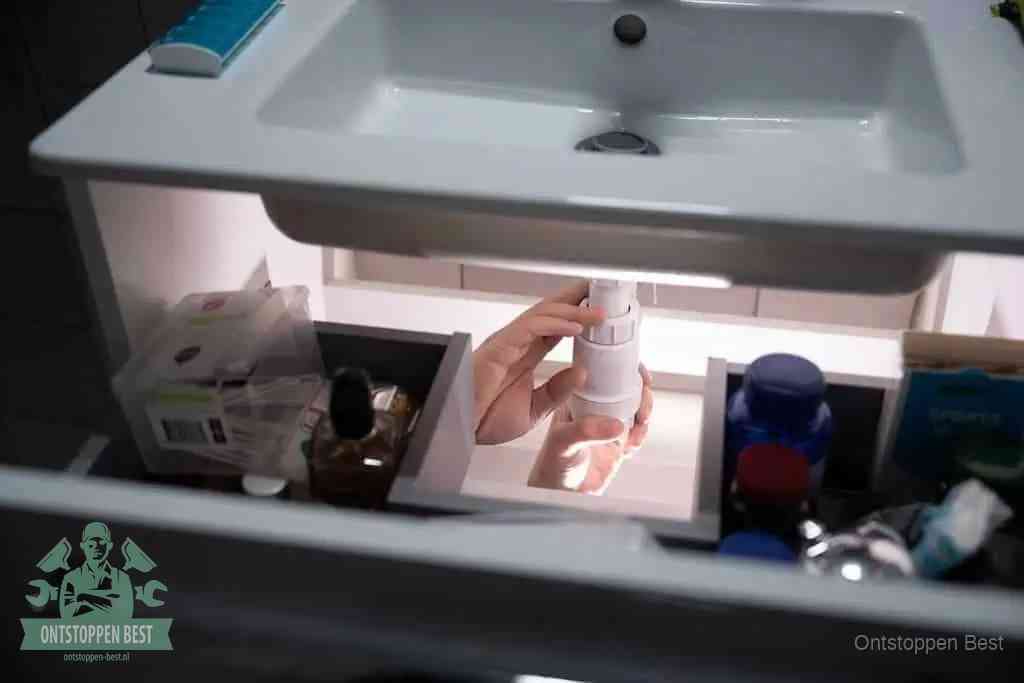Een pompfles met zeep boven een wastafel in de toiletruimte, de warm water en afwasmiddel-methode om de wc te ontstoppen in Best