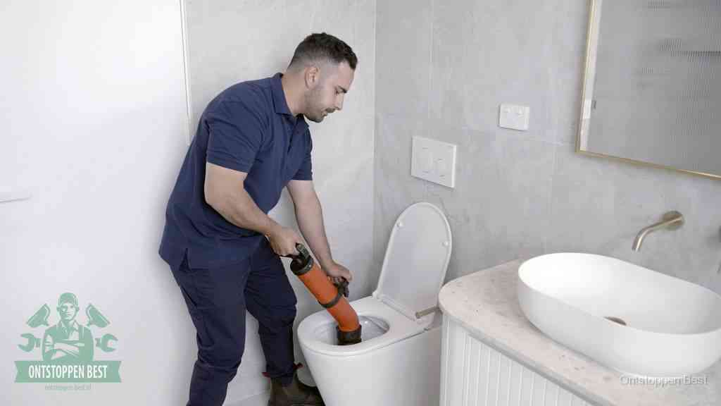Een man gebruikt een handmatige luchtdruk-ontstopper in een modern betegeld toilet om zelf de wc te ontstoppen in Best